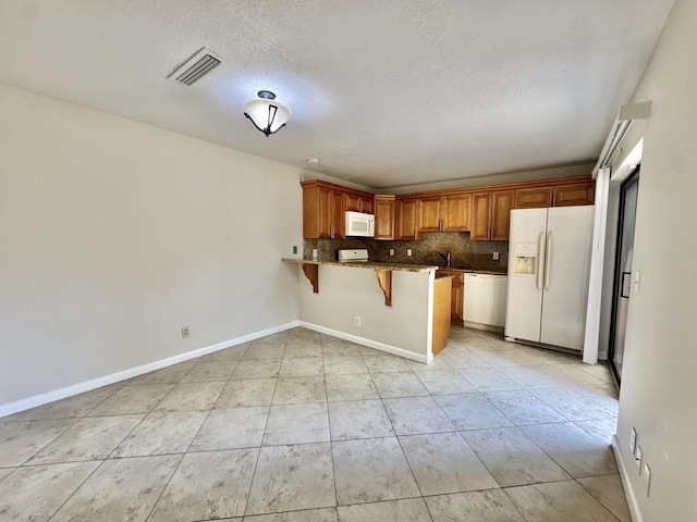 kitchen featuring tasteful backsplash, visible vents, white appliances, a peninsula, and a kitchen breakfast bar