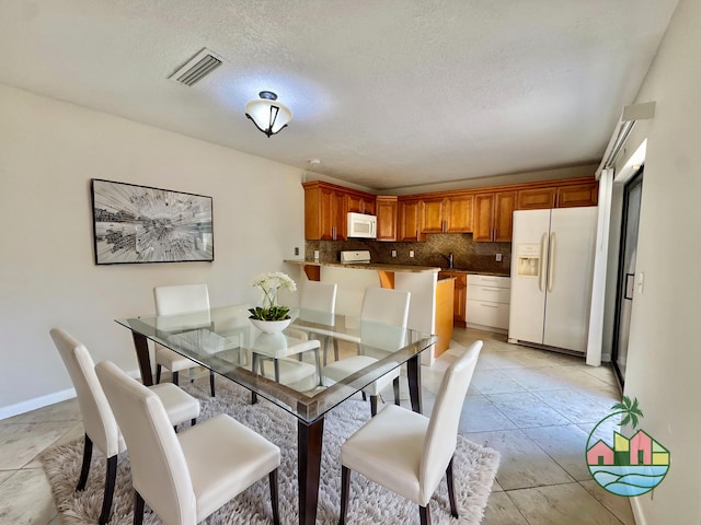 dining area featuring light tile patterned floors, baseboards, visible vents, and a textured ceiling