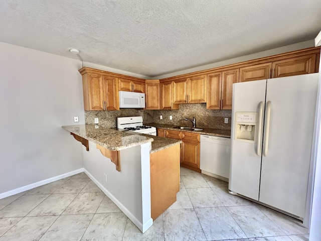 kitchen with white appliances, dark stone counters, brown cabinets, a sink, and backsplash