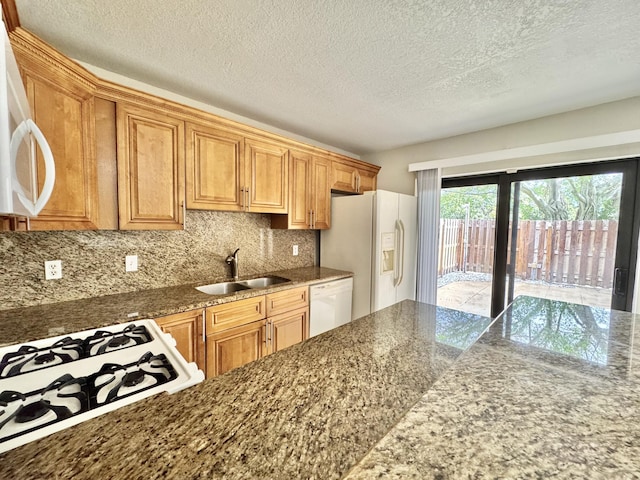 kitchen featuring dark stone counters, white appliances, a sink, and decorative backsplash