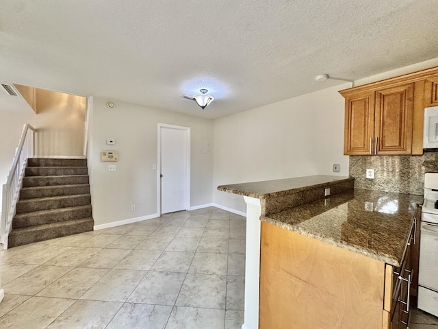 kitchen with white appliances, baseboards, decorative backsplash, brown cabinets, and dark stone counters