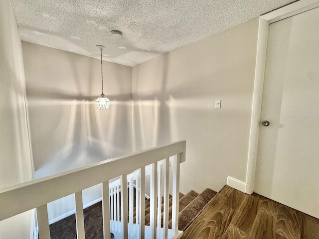 stairway with a textured ceiling, wood finished floors, and baseboards