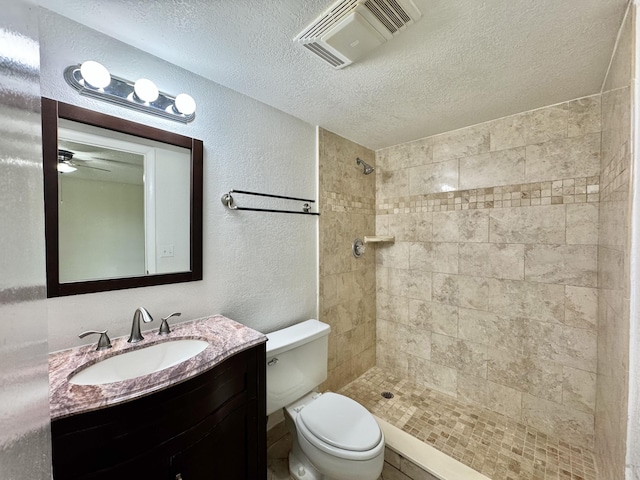 bathroom with visible vents, a textured wall, toilet, a tile shower, and vanity