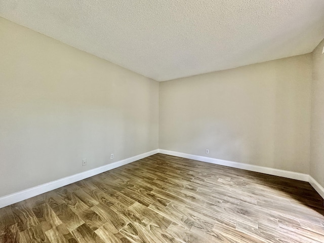 spare room with a textured ceiling, baseboards, and wood finished floors