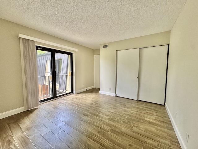 unfurnished bedroom with baseboards, wood finished floors, visible vents, and access to exterior