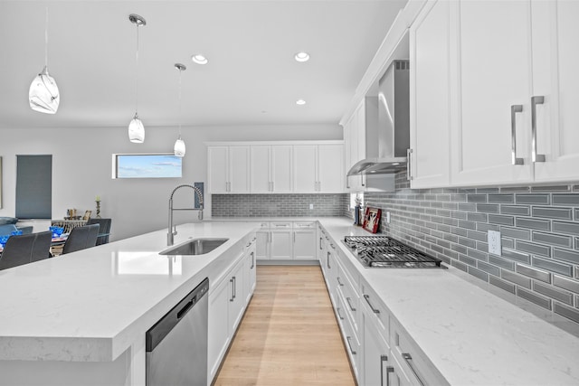 kitchen featuring sink, appliances with stainless steel finishes, pendant lighting, wall chimney range hood, and white cabinets