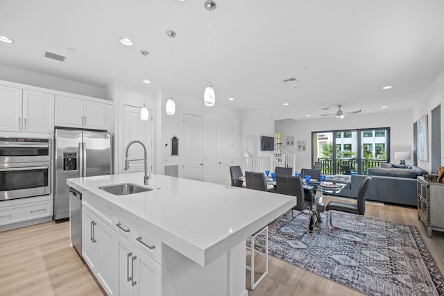 kitchen featuring appliances with stainless steel finishes, pendant lighting, white cabinetry, sink, and a kitchen island with sink