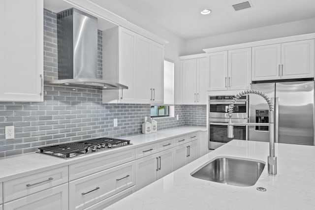 kitchen with stainless steel appliances, white cabinetry, light stone countertops, and wall chimney exhaust hood