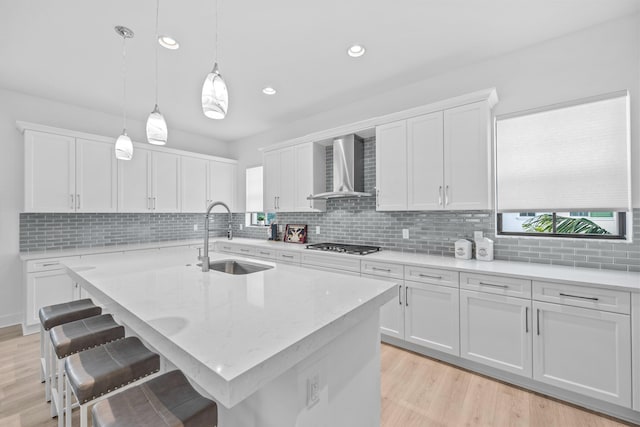 kitchen with white cabinets, an island with sink, sink, and wall chimney range hood