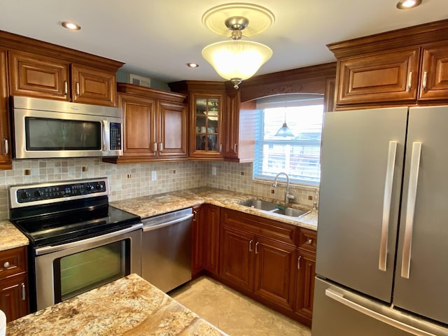 kitchen featuring stainless steel appliances, light stone countertops, hanging light fixtures, and sink