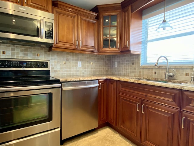 kitchen featuring decorative light fixtures, sink, decorative backsplash, light stone counters, and stainless steel appliances