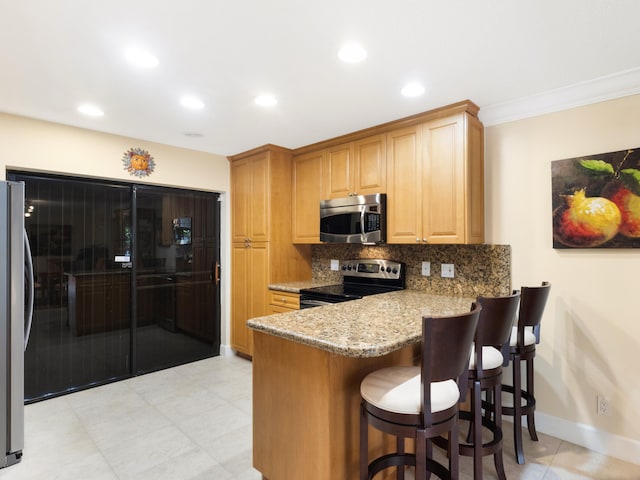kitchen with appliances with stainless steel finishes, a breakfast bar, decorative backsplash, light stone counters, and kitchen peninsula