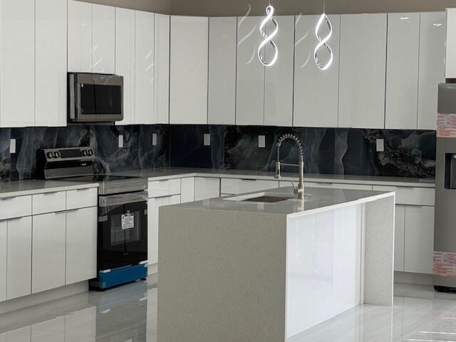 kitchen featuring sink, appliances with stainless steel finishes, a kitchen island with sink, tasteful backsplash, and white cabinets