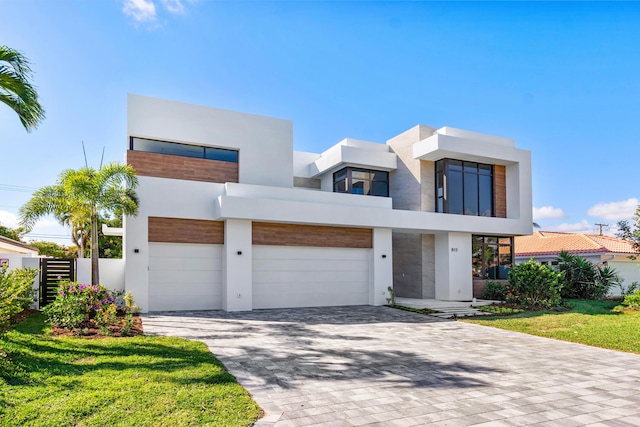 modern home featuring a garage, stucco siding, fence, and decorative driveway