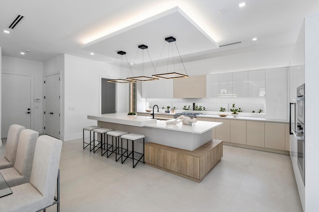 kitchen with pendant lighting, a breakfast bar area, white cabinetry, a center island with sink, and stainless steel oven