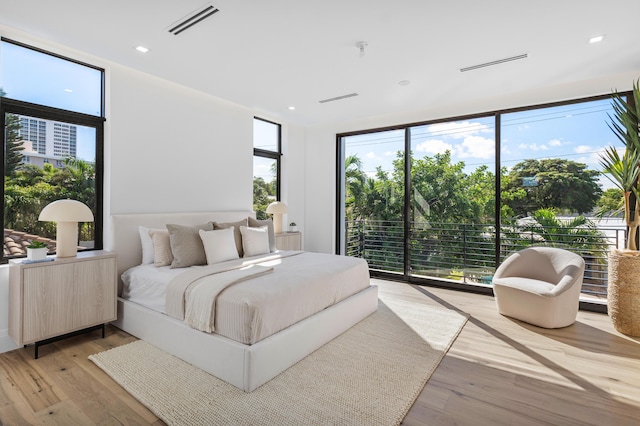 bedroom featuring multiple windows, access to outside, light wood-type flooring, and a wall of windows