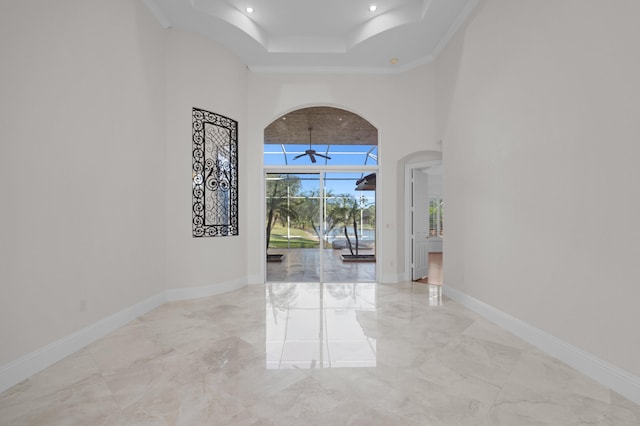 foyer featuring arched walkways, marble finish floor, a towering ceiling, and baseboards