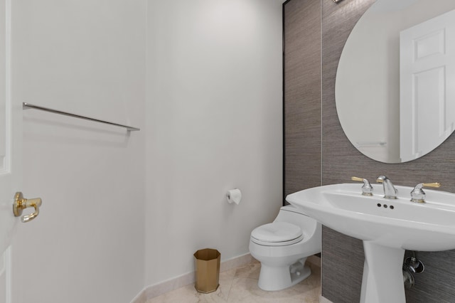 half bath with baseboards, a sink, toilet, and tile patterned floors