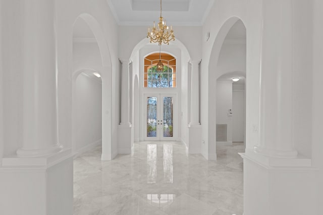 foyer with a towering ceiling, marble finish floor, french doors, ornate columns, and a chandelier