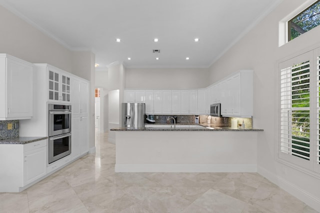 kitchen with dark stone counters, a towering ceiling, ornamental molding, stainless steel appliances, and white cabinetry