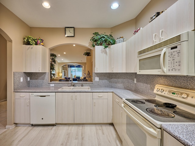 kitchen with sink, light wood-type flooring, backsplash, light brown cabinets, and white appliances