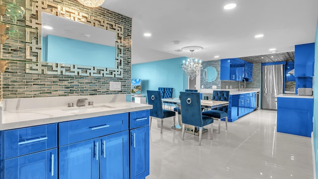 kitchen with sink, stainless steel fridge, pendant lighting, light stone countertops, and backsplash