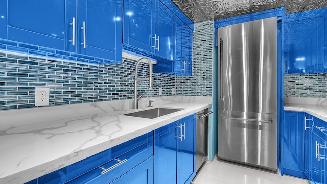 kitchen with sink, blue cabinetry, appliances with stainless steel finishes, tasteful backsplash, and light stone countertops