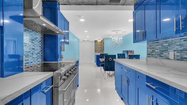 kitchen featuring blue cabinets, light stone countertops, high end stainless steel range oven, range hood, and backsplash