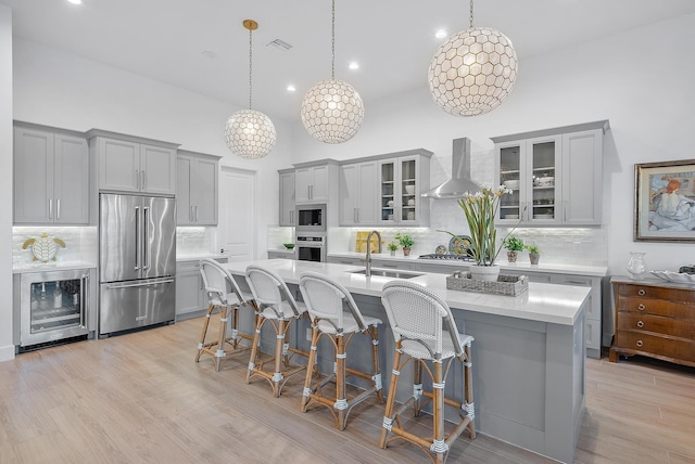 kitchen featuring stainless steel appliances, an island with sink, sink, and wall chimney exhaust hood