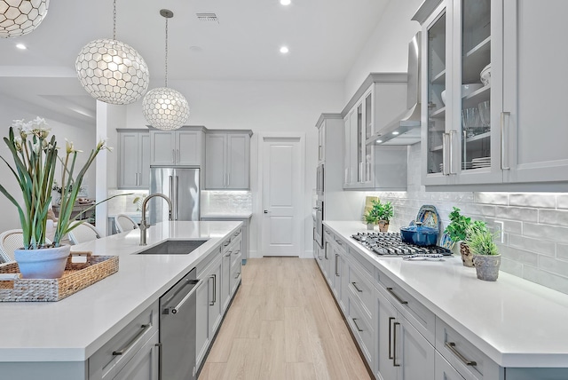 kitchen featuring sink, hanging light fixtures, gray cabinets, stainless steel appliances, and wall chimney range hood