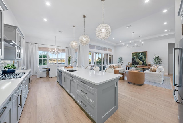 kitchen featuring gray cabinetry, a kitchen island with sink, hanging light fixtures, and a notable chandelier