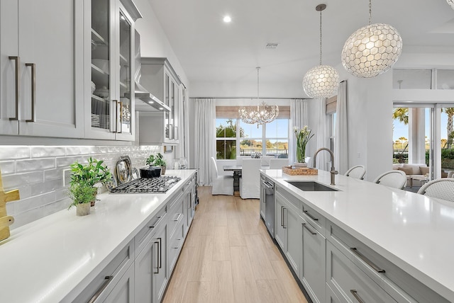 kitchen featuring sink, gray cabinetry, hanging light fixtures, decorative backsplash, and a chandelier