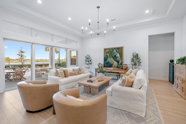 living room with a notable chandelier, a tray ceiling, and light wood-type flooring