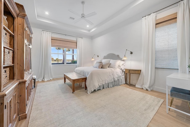 bedroom with a tray ceiling, light hardwood / wood-style floors, and ceiling fan