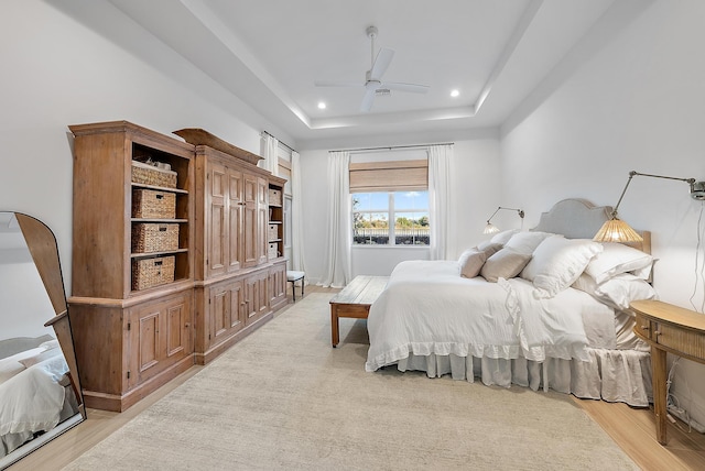 bedroom with ceiling fan, a tray ceiling, and light hardwood / wood-style flooring