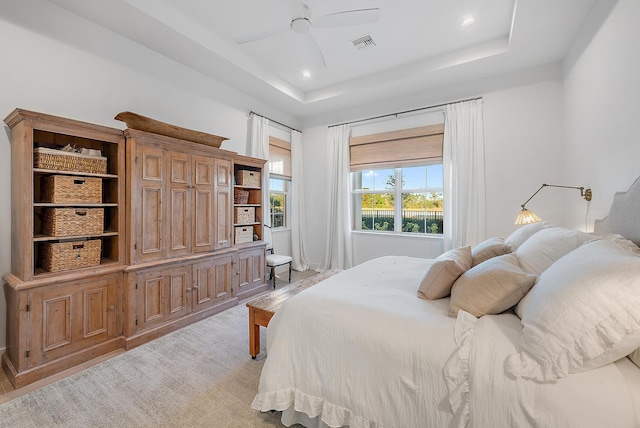 bedroom with a raised ceiling, light carpet, and ceiling fan