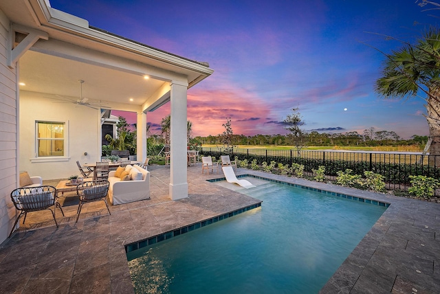 pool at dusk featuring a patio, an outdoor hangout area, and ceiling fan