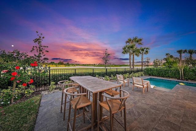 patio terrace at dusk with a fenced in pool