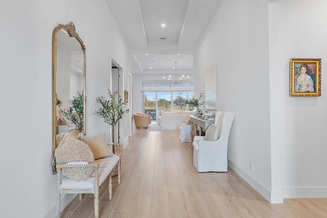 hall featuring an inviting chandelier, light hardwood / wood-style flooring, and a raised ceiling