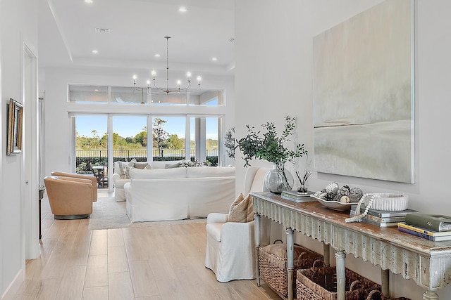 living room featuring a towering ceiling, a notable chandelier, light hardwood / wood-style floors, and a tray ceiling