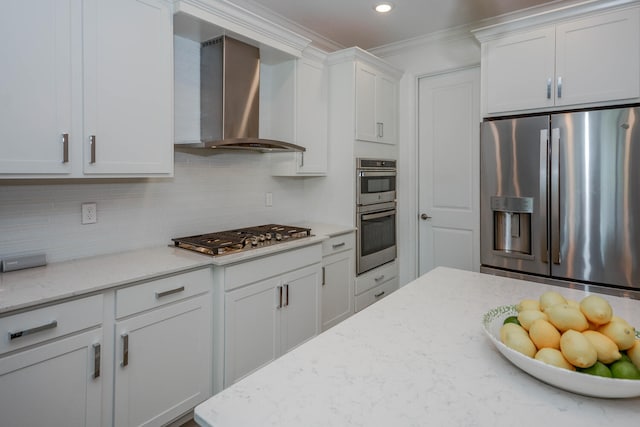 kitchen with appliances with stainless steel finishes, light stone counters, wall chimney range hood, white cabinetry, and backsplash