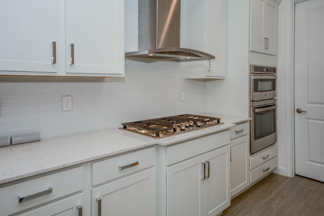 kitchen with light stone countertops, white cabinetry, appliances with stainless steel finishes, decorative backsplash, and wall chimney exhaust hood