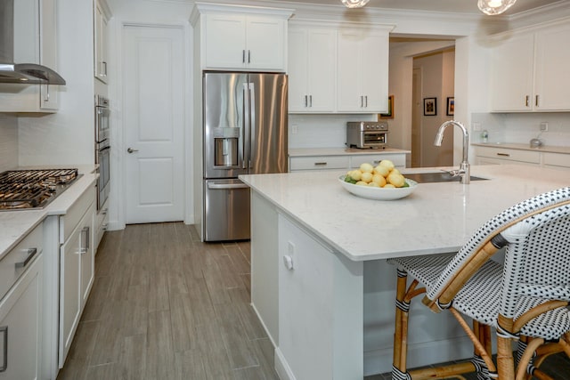 kitchen with light stone counters, appliances with stainless steel finishes, light wood-style floors, white cabinetry, and wall chimney exhaust hood