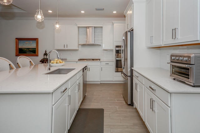 kitchen with a center island with sink, appliances with stainless steel finishes, a sink, wall chimney range hood, and light stone countertops