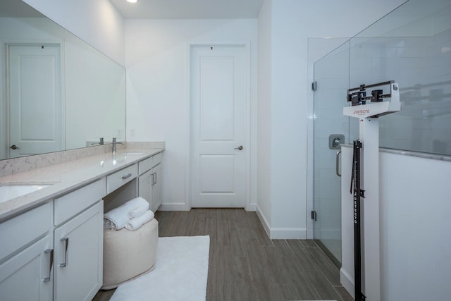 bathroom with double vanity, a stall shower, baseboards, wood finished floors, and a sink