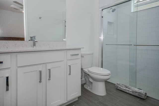 bathroom featuring toilet, a ceiling fan, vanity, wood tiled floor, and a stall shower