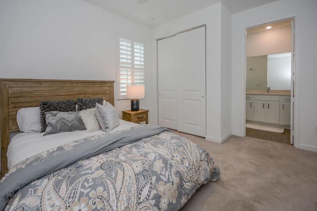 bedroom with a closet, baseboards, light colored carpet, ensuite bathroom, and a sink