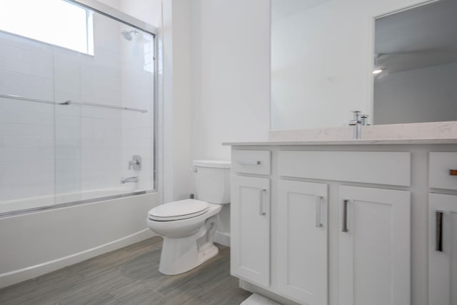 bathroom with toilet, wood finished floors, vanity, baseboards, and combined bath / shower with glass door