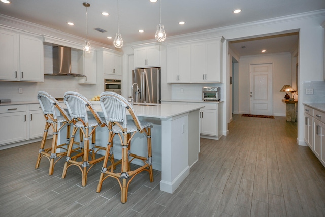 kitchen featuring stainless steel appliances, wall chimney range hood, a center island with sink, and white cabinets