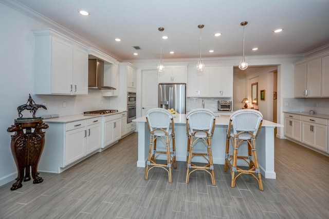 kitchen with light countertops, hanging light fixtures, appliances with stainless steel finishes, white cabinets, and wall chimney range hood